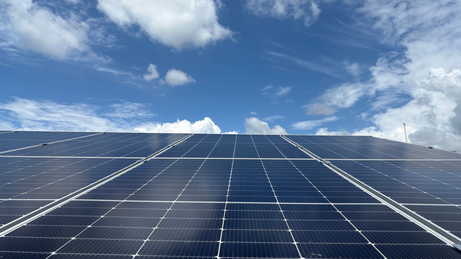 Rows of solar panels under a blue sky with clouds