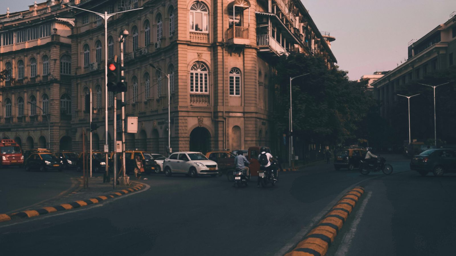 Stone colonial-era buildings along a road at dusk with vehicles and a traffic signal