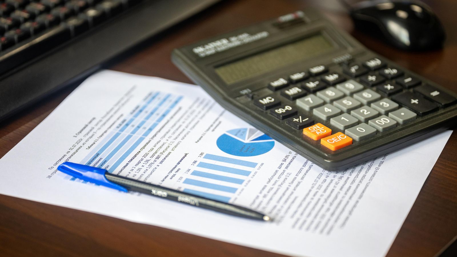 Calculator and pen on a printed report with bar and pie charts