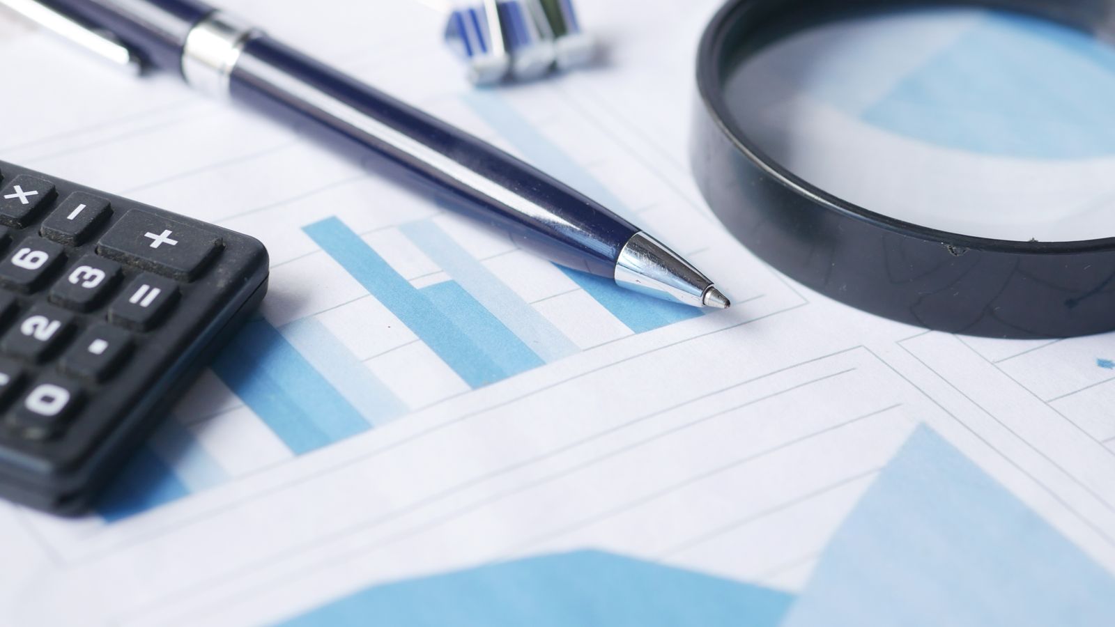 Pen, calculator and magnifying glass on printed documents with charts