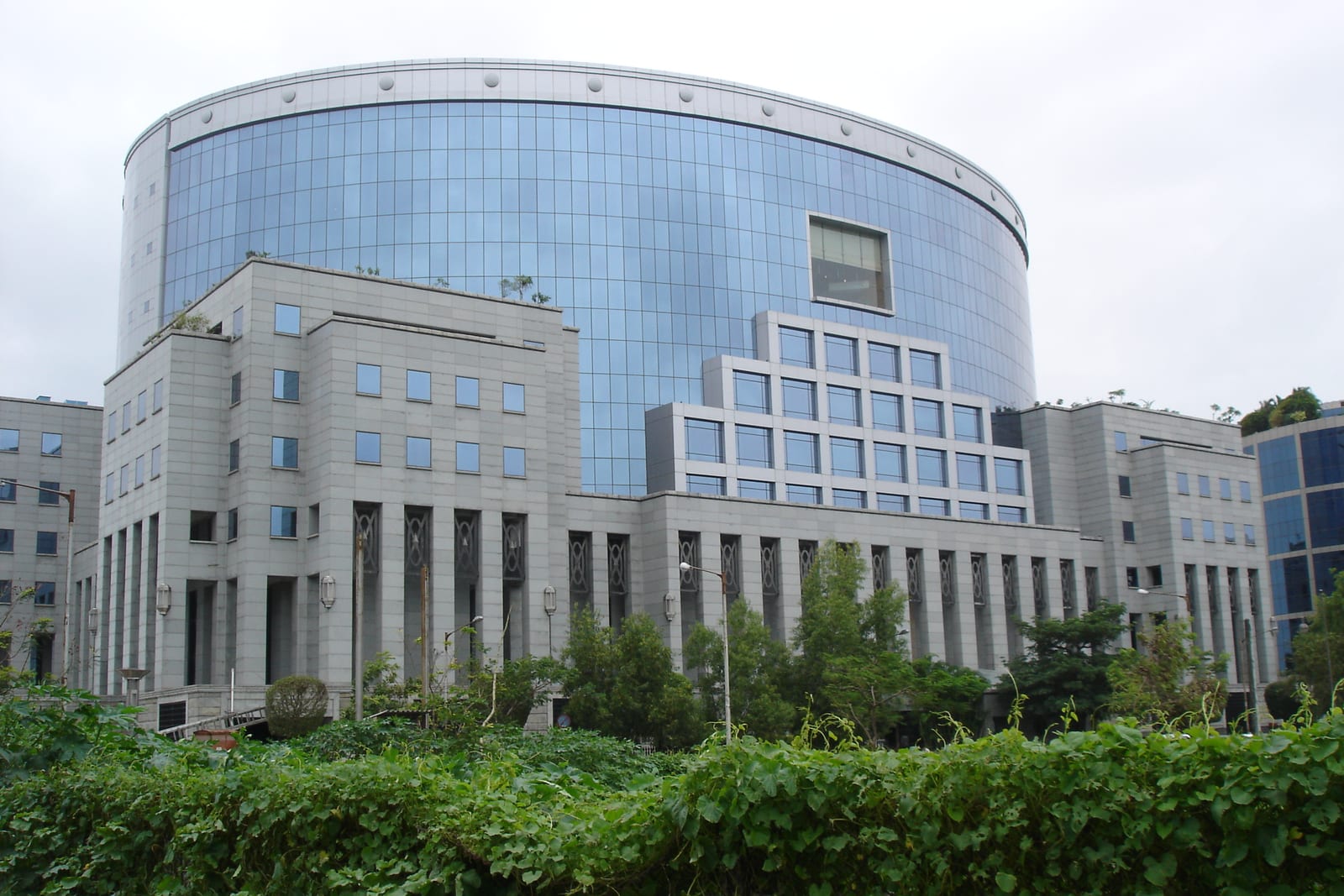 Curved glass office building with a stepped stone base and green foliage in front