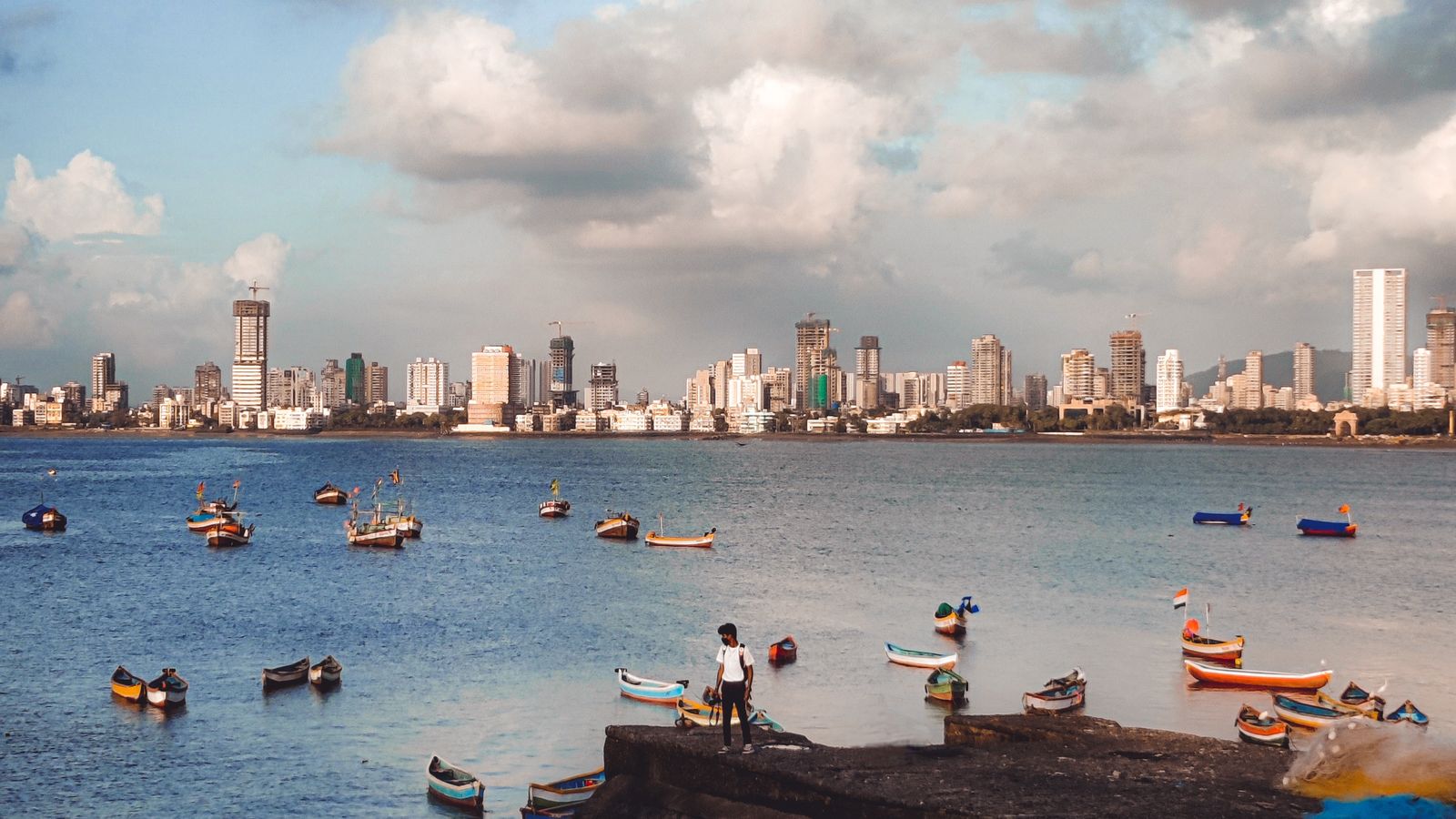 Small boats on a bay in front of a dense city skyline under a cloudy sky