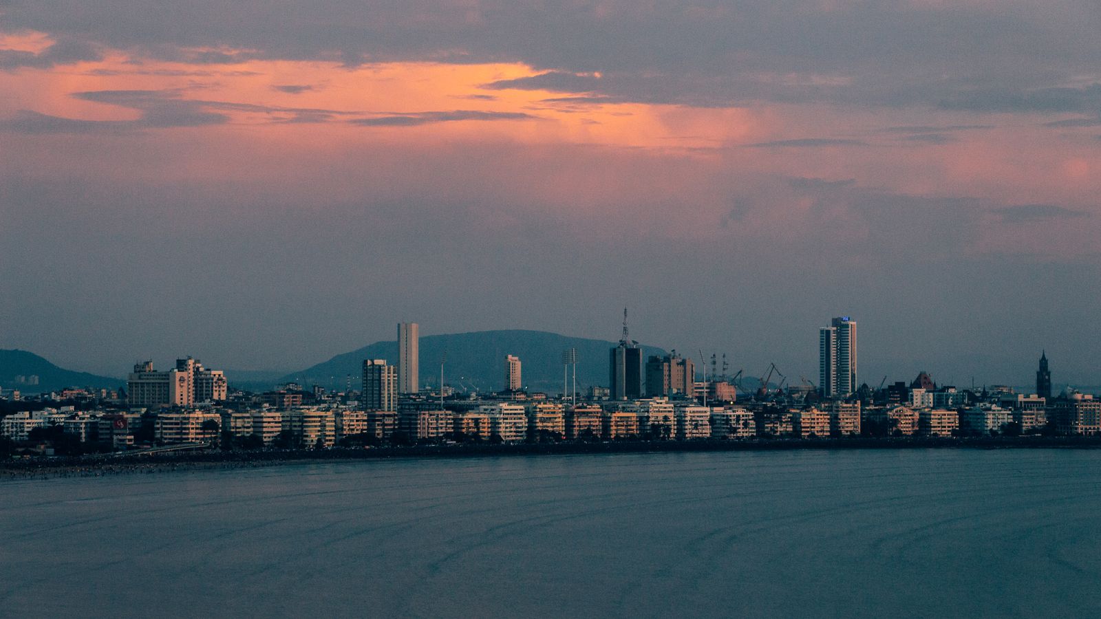 City skyline across the water at dusk with hills in the distance