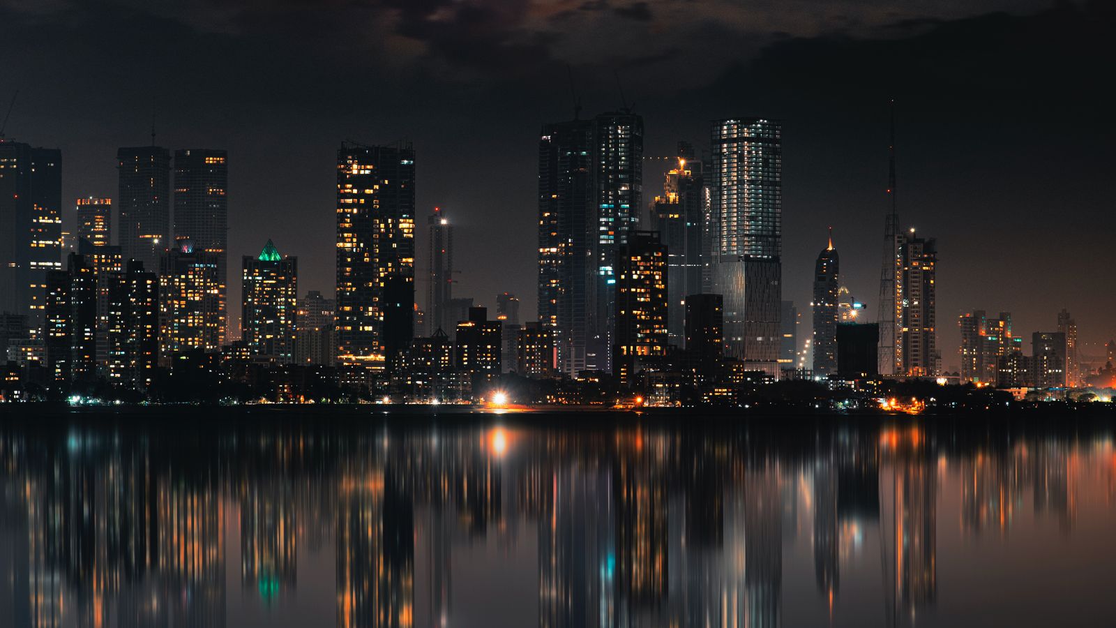 City towers lit at night, reflected in the water in front of them