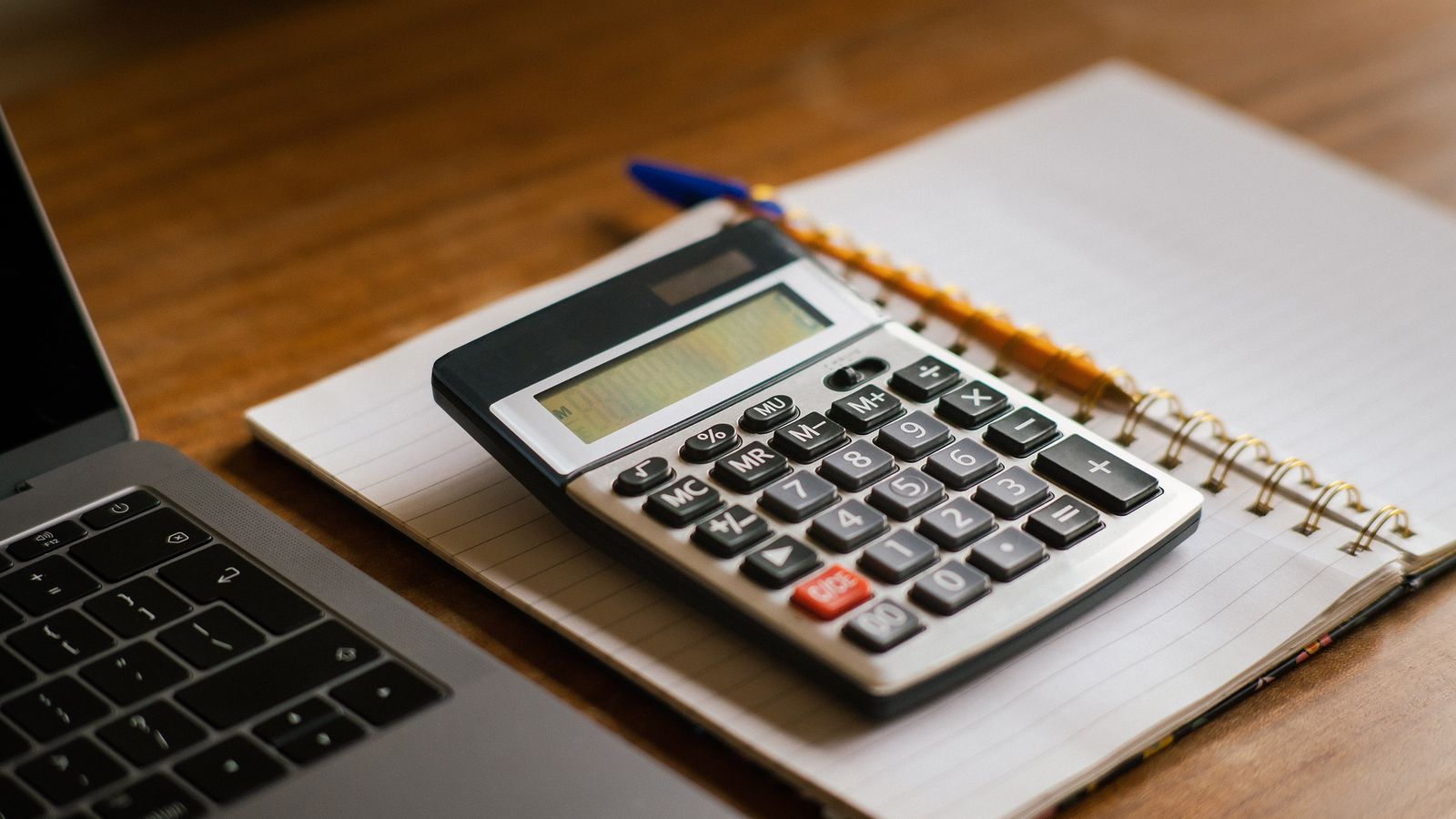 Calculator resting on a notebook beside an open laptop on a wooden desk