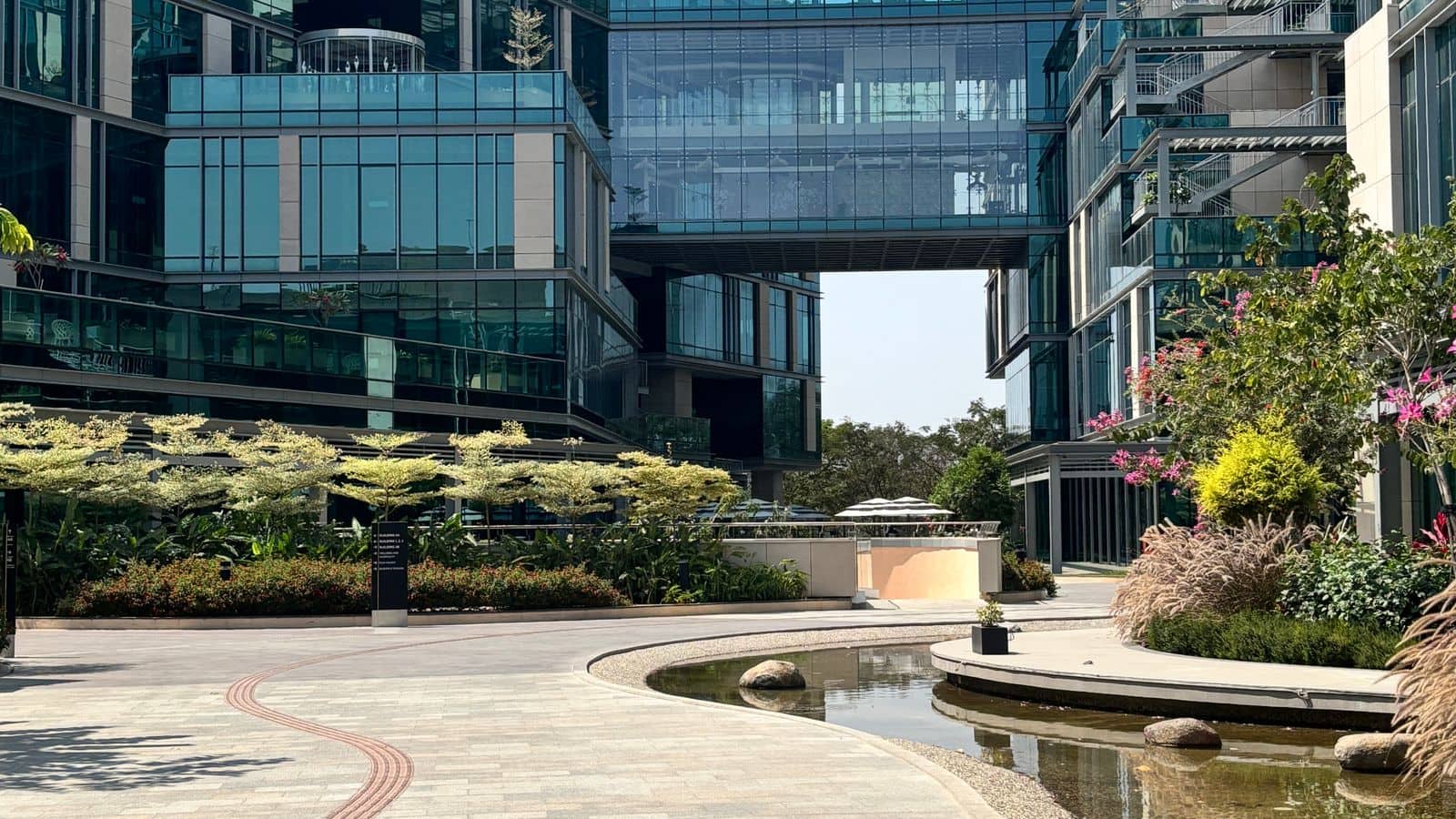 Glass office towers linked by a bridge above a landscaped courtyard with a water feature