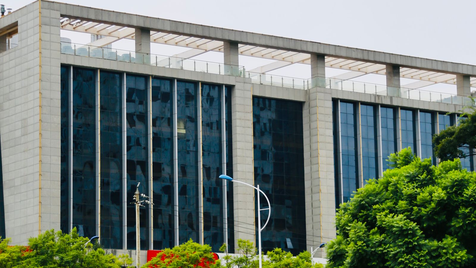 Glass-fronted office block with concrete columns and trees in front